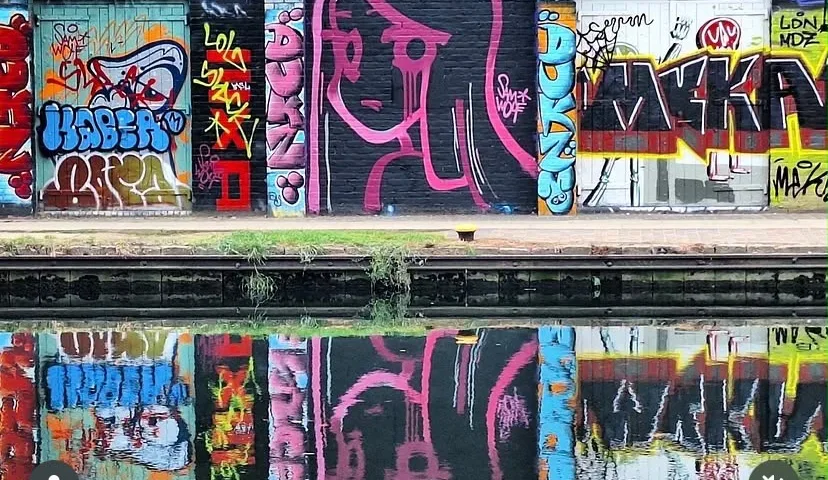 Graffiti lettering and pink outlined portrait along a waterside wall reflected in the water