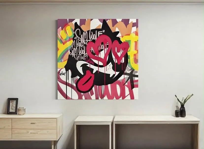 Bright graffiti-style canvas with pink hearts displayed on a white wall above wooden furniture