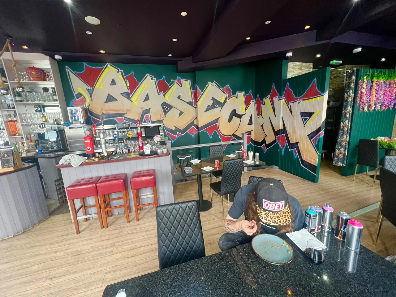 Gold graffiti lettering across the walls of a café or restaurant interior with painting materials in the foreground