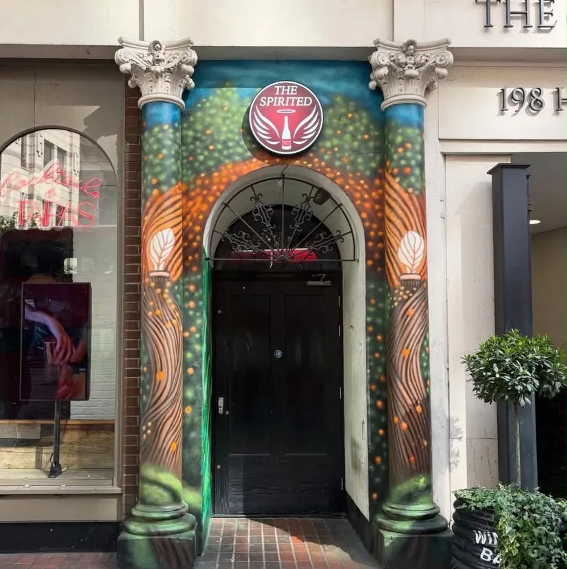The Spirited entrance framed by blue painted columns and a colourful foliage mural