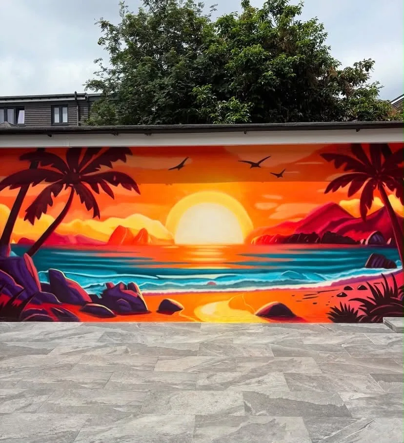 Bright orange sunset, palm trees, sea and mountains painted across an outdoor wall